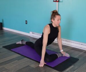 Dr. Chloe in full pigeon stretch with her right shin parallel to the front of the mat, left leg stretched behind her 